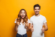 © Drobot Dean - Image of happy young people man and woman in basic clothing laughing and showing thumbs up at camera, isolated over yellow background