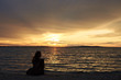 © anatoliy_gleb - Back view silhouette of female tourist with backpack sitting alone on seashore at water edge, enjoying beautiful view of sunset on dark evening sky background. Tourism and vacations concept.