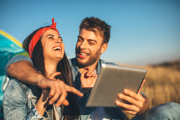 Happy young couple uses a digital tablet on sunny day in nature