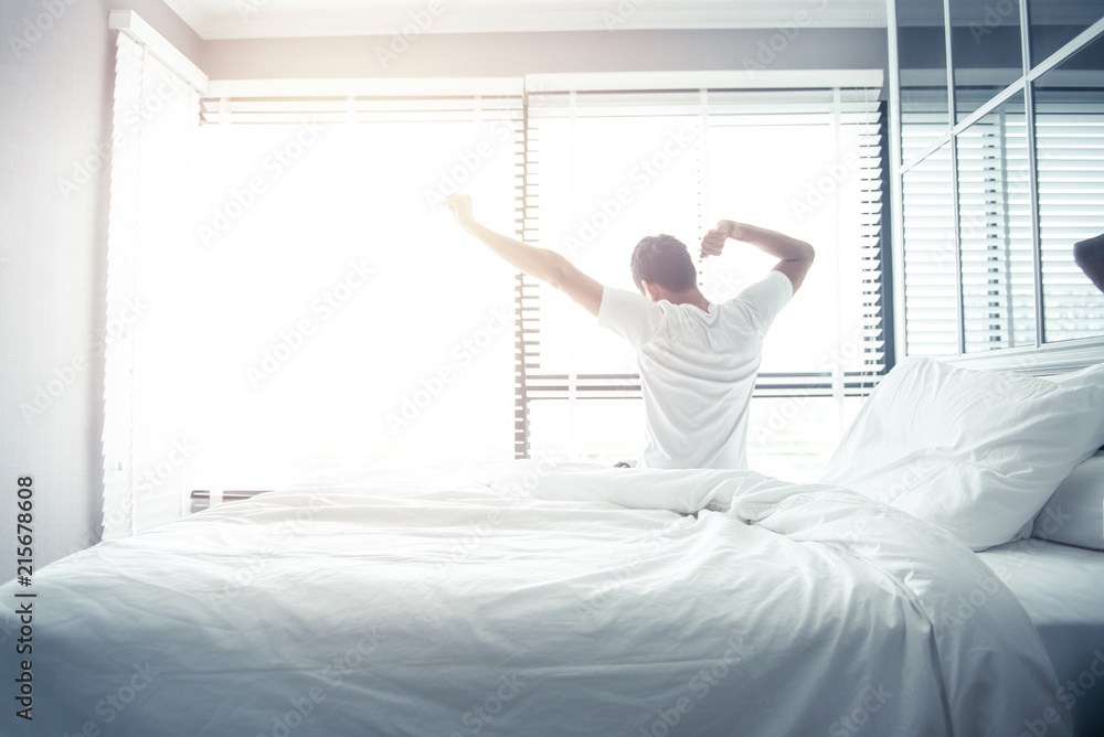 Man wake up and stretching on bed in morning with sunlight - obrazy, fototapety, plakaty 