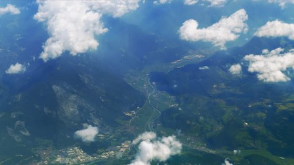 Wall Mural - Flying over green mountain valley in pure sunshine with fluffy clouds passing by. Picturesque view from airplane window to beautiful green hills, villages and rivers far beneath.