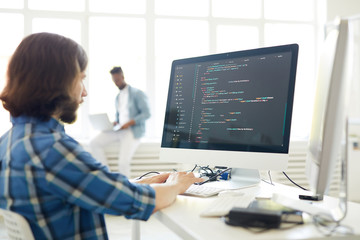 serious busy hipster young web developer typing on computer keyboard while coding information in mod