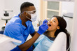 Close-up portrait of the african young woman patient examining by male dentist with tools in dental clinic.