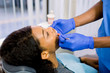 © sofiko14 - Young african american woman lying in chair receiving dental treatment with mouth open, dentist hands wearing gloves holding tools working on patients teeth