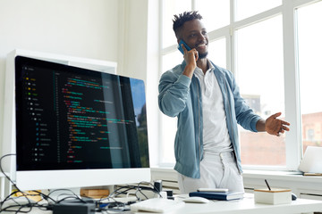 Sticker - cheerful successful young african-american freelance coder with beard gesturing while talking on pho