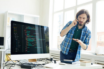 Wall Mural - puzzled handsome hipster young it specialist in casual outfit asking question to customer on phone w
