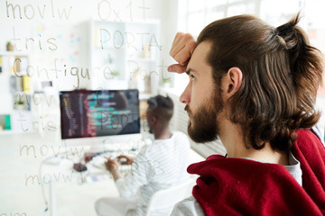 Wall Mural - serious confused hipster coder with pony tail looking at computer text while brainstorming about sol
