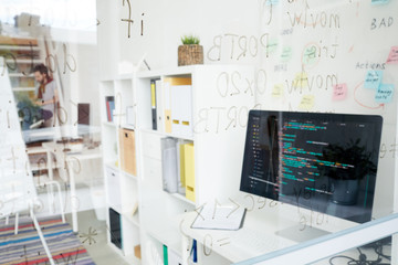 Wall Mural - Coders workplace: glassy wall with script language, desktop computer with code on table, marketing board behind computer, hipster man working in background