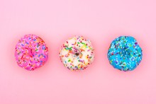 Three Assorted Donuts With Pastel Colored Icing And Sprinkles Against A Soft Pink Background. Minimal Concept.
