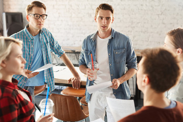 Group of creative young professionals discussing ideas while collaborating during meeting in modern office or cafe, focus on handsome young man holding smoothie