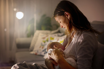 Young beautiful mother, breastfeeding her newborn baby boy at night