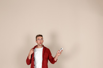 Canvas Print - Young man operating air conditioner with remote control on light background