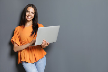 Young woman with modern laptop on grey background