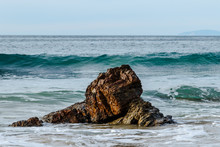 Wave Cresting Behind Rock Near The Beach Of Crystal Cove State Park In Laguna Beach, California. Foam From An Earlier Wave Is In The Foreground; Pacific Ocean Is In The Background.