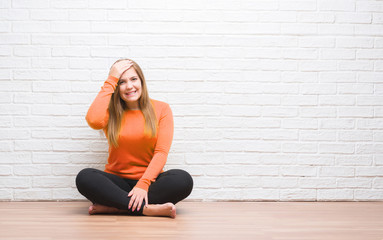 Canvas Print - Young adult woman sitting on the floor in autumn over white brick wall stressed with hand on head, shocked with shame and surprise face, angry and frustrated. Fear and upset for mistake.