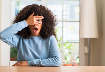 Poster - African american woman at home peeking in shock covering face and eyes with hand, looking through fingers with embarrassed expression.