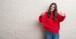© Krakenimages.com - Young brunette woman standing over white brick wall approving doing positive gesture with hand, thumbs up smiling and happy for success. Looking at the camera, winner gesture.