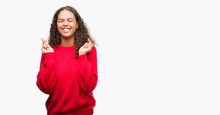 Young Hispanic Woman Wearing Red Sweater Smiling Crossing Fingers With Hope And Eyes Closed. Luck And Superstitious Concept.