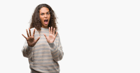 Beautiful young hispanic woman wearing stripes sweater afraid and terrified with fear expression stop gesture with hands, shouting in shock. Panic concept.