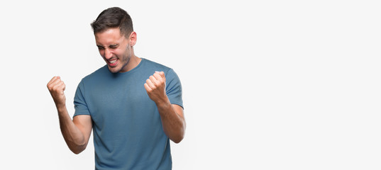 Canvas Print - Handsome young casual man very happy and excited doing winner gesture with arms raised, smiling and screaming for success. Celebration concept.