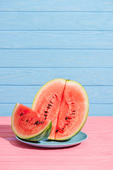 Wall Mural - close up view of cut juicy watermelon on plate on pink tabletop on blue backdrop