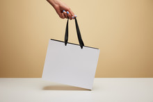 Cropped Image Of Woman Holding White Shopping Bag Above White Table Isolated On Beige