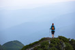 © Vitalii_Mamchuk - The tourist girl with the tracking sticks and the back sack at the edge of the cliff. The landscape with the high mountains. Endless vastness on the horizon. Warm sunny summer day.