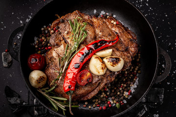 concept of the process of cooking meat. The steak is roasted on charcoal in a cast-iron frying pan, with spices, garlic, hot red pepper, squarish, thyme. image background. Copy space, selective focus