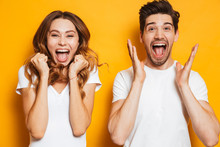 Photo Of Beautiful Admired Couple Man And Woman In Basic Clothing Screaming In Surprise Or Delight And Touching Cheeks, Isolated Over Yellow Background