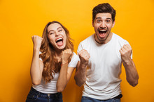 Portrait Of Positive Beautiful Man And Woman In Basic Clothing Screaming And Clenching Fists Like Winners Or Happy People, Isolated Over Yellow Background
