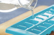 © dubravina - Pouring water into ice cube tray on the kitchen table.