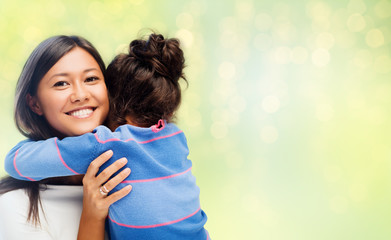 family, motherhood and people concept - happy mother and daughter hugging over green holidays lights