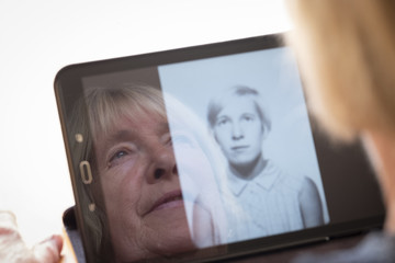 Senior caucasian woman looking at old photos of herself as a young woman on a tablet computer themes of contrasts the ageing process nostalgia and childhood