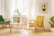 © Photographee.eu - Yellow, retro armchair and a green sofa by a big, sunny window in a stylish, white real living room interior with a poster on the wall