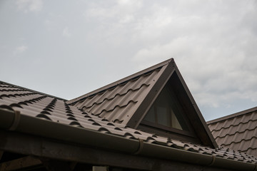 Wall Mural - Modern roof covered with tile effect PVC coated brown metal roof sheets against cloudy sky.