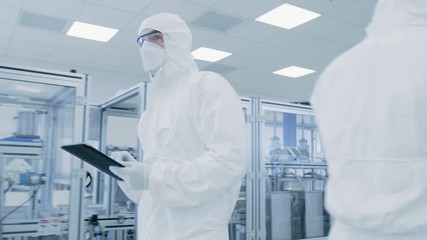 Wall Mural - Quality Control Check: Scientist Using Digital Tablet Computer and wearing Protective Suit walks through Manufacturing Laboratory