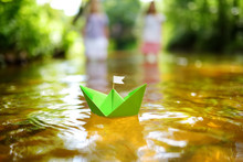 Two Little Sisters Playing With Paper Boats By A River On Warm And Sunny Summer Day. Children Having Fun By The Water.