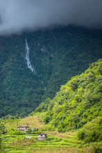 Waterfall In Lush Green Forest Of Annapurna With Small Village Below. 