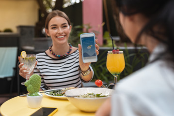 Wall Mural - Weather forecast. Smiling woman showing weather forecast on her phone while planning trip