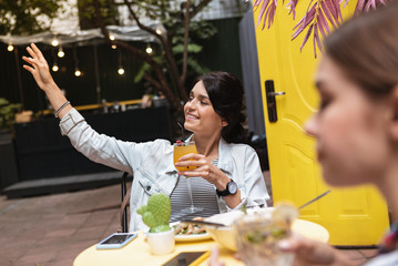 Wall Mural - Calling waiter. Dark-haired fashionable businesswoman lifting her hand while calling waiter in cafeteria