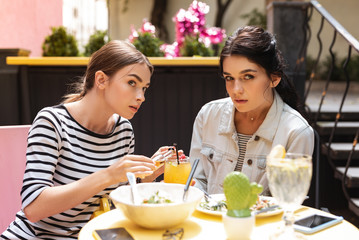 Wall Mural - Secret alcohol. Two young women secretly adding alcohol from little bottle to their cocktail from restaurant
