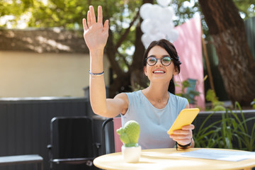 Wall Mural - Calling waiter. Pleasant good-looking woman wearing glasses lifting her hand while calling waiter
