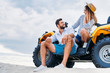 © LIGHTFIELD STUDIOS - happy young couple sitting on ATV on sandy dune in front of cloudy sky
