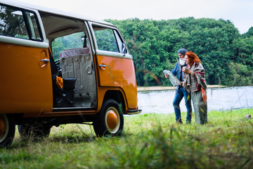 An old hipster couple looks at a road map by their camper van 