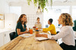 © Bonninstudio/Stocksy - Female co-workers eating an snack whilst working at office.