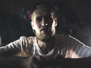 Wall Mural - young bearded man close up portrait playing video game holding gaming controller joystick gamepad in dark room