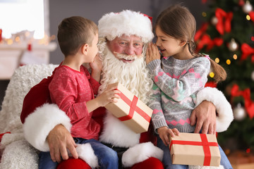 Poster - Little children with gift boxes sitting on authentic Santa Claus' knees indoors