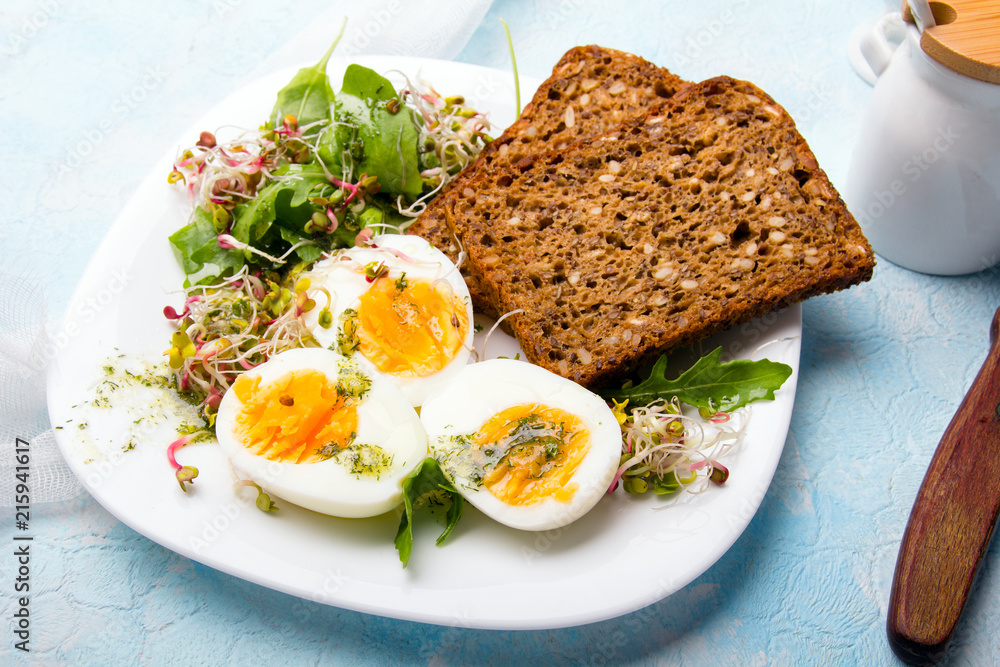Zdrowe śniadanie: Jajka gotowane na twardo, świeże kiełki, rukola i kromka pełnoziarnistego chleba  na niebieskim tle, miejsce na tekst.  - obrazy, fototapety, plakaty 