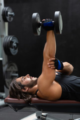 Fit strong man lifting a heavy dumbbell in a gym