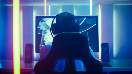 Wall Mural - Back View Shot of the Professional Gamer Playing in First-Person Shooter Online Video Game on His Personal Computer. Room Lit by Neon Lights in Retro Arcade Style. Online Cyber e-Sport Internet.